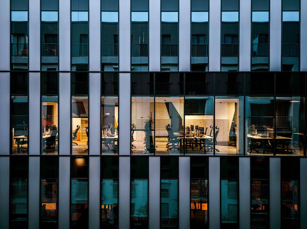 Glasfassade eines Bürohauses am Abend, ein Stockwerk ist erleuchtet